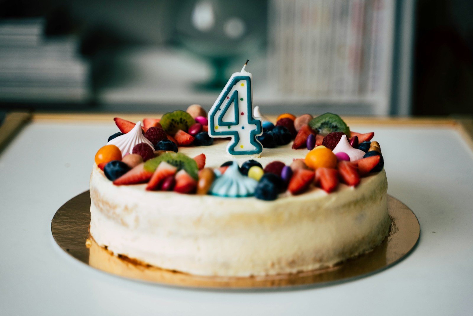 Cream birthday cake topped with fresh fruit and a number four candle