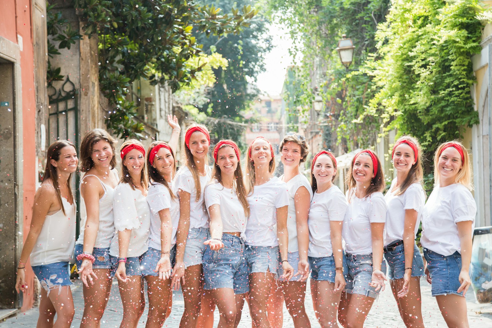 Despedida de soltera con camisetas blancas, pañuelos rojos y confeti en una calle empedrada