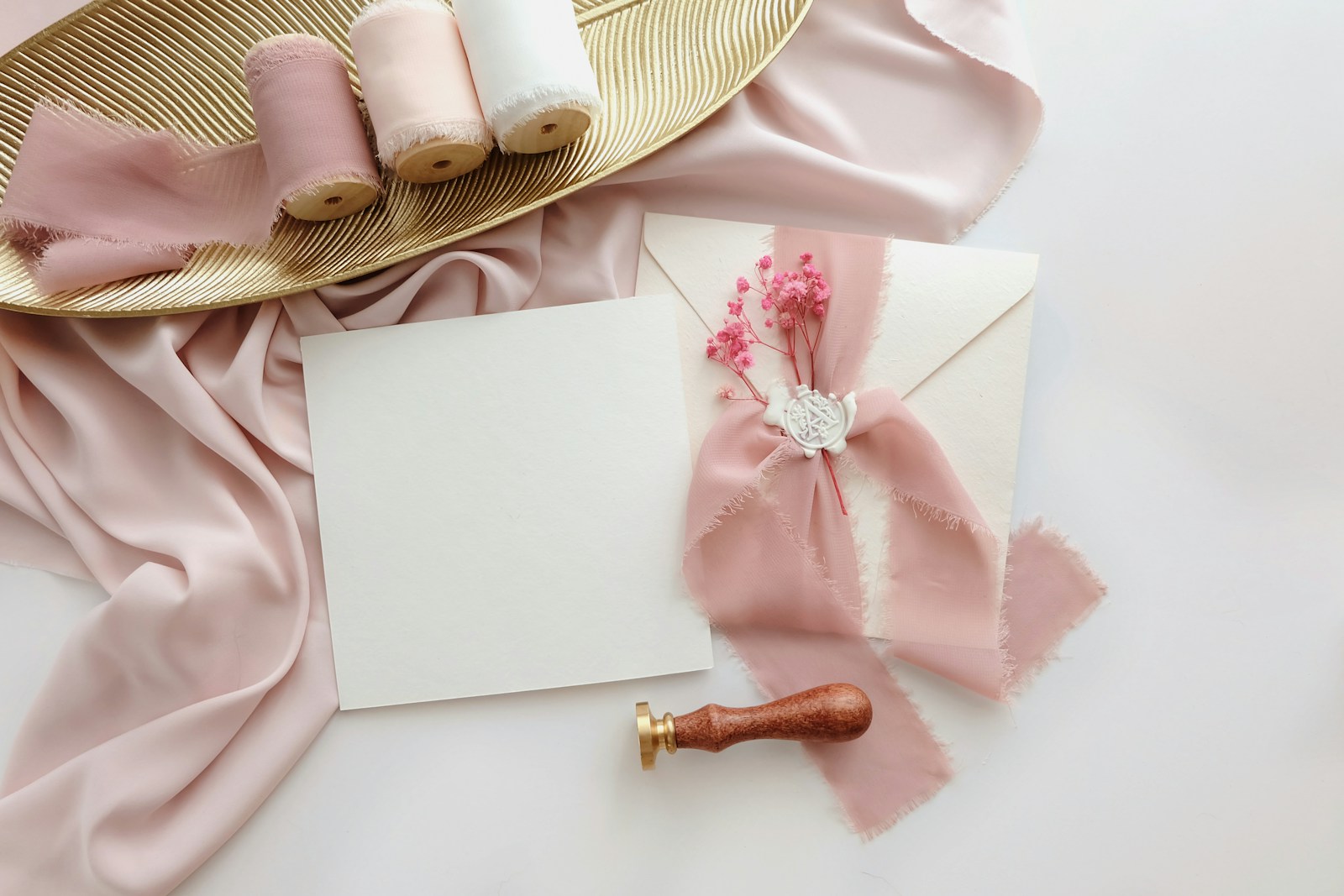 Blanco kaart naast een envelop met roze zijden lint en een lakzegel