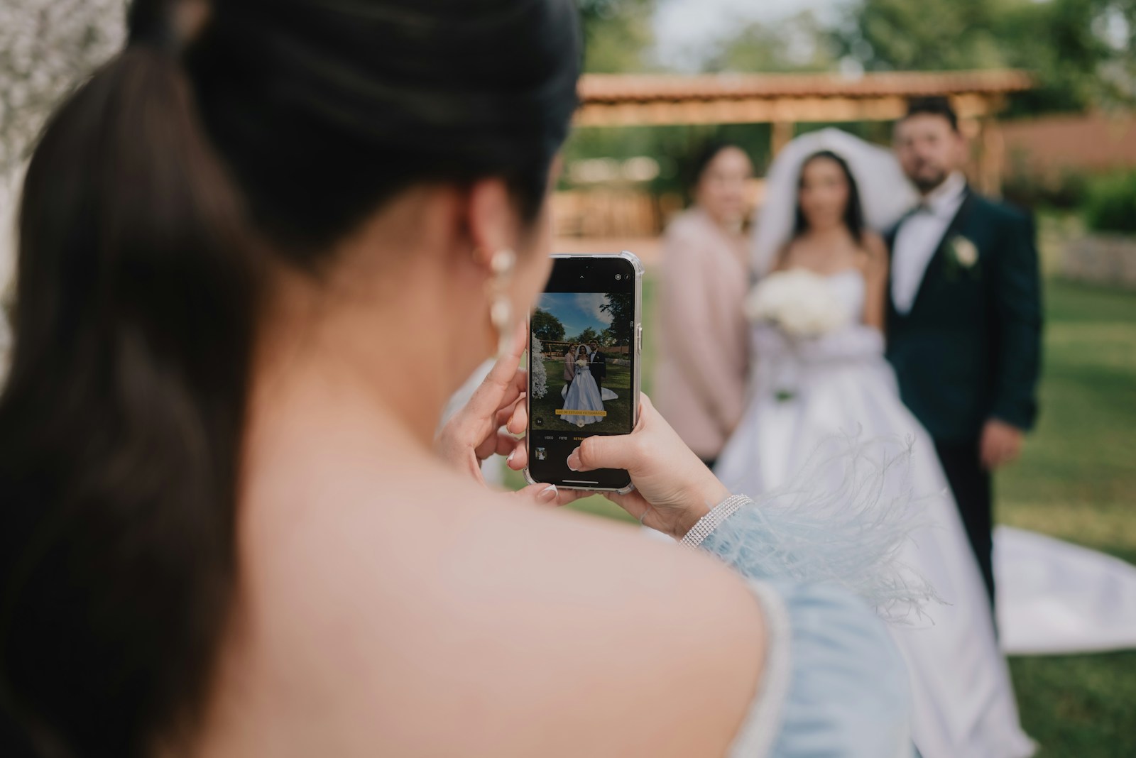 Ein Gast fotografiert das Brautpaar mit dem Handy in einem sonnigen Garten