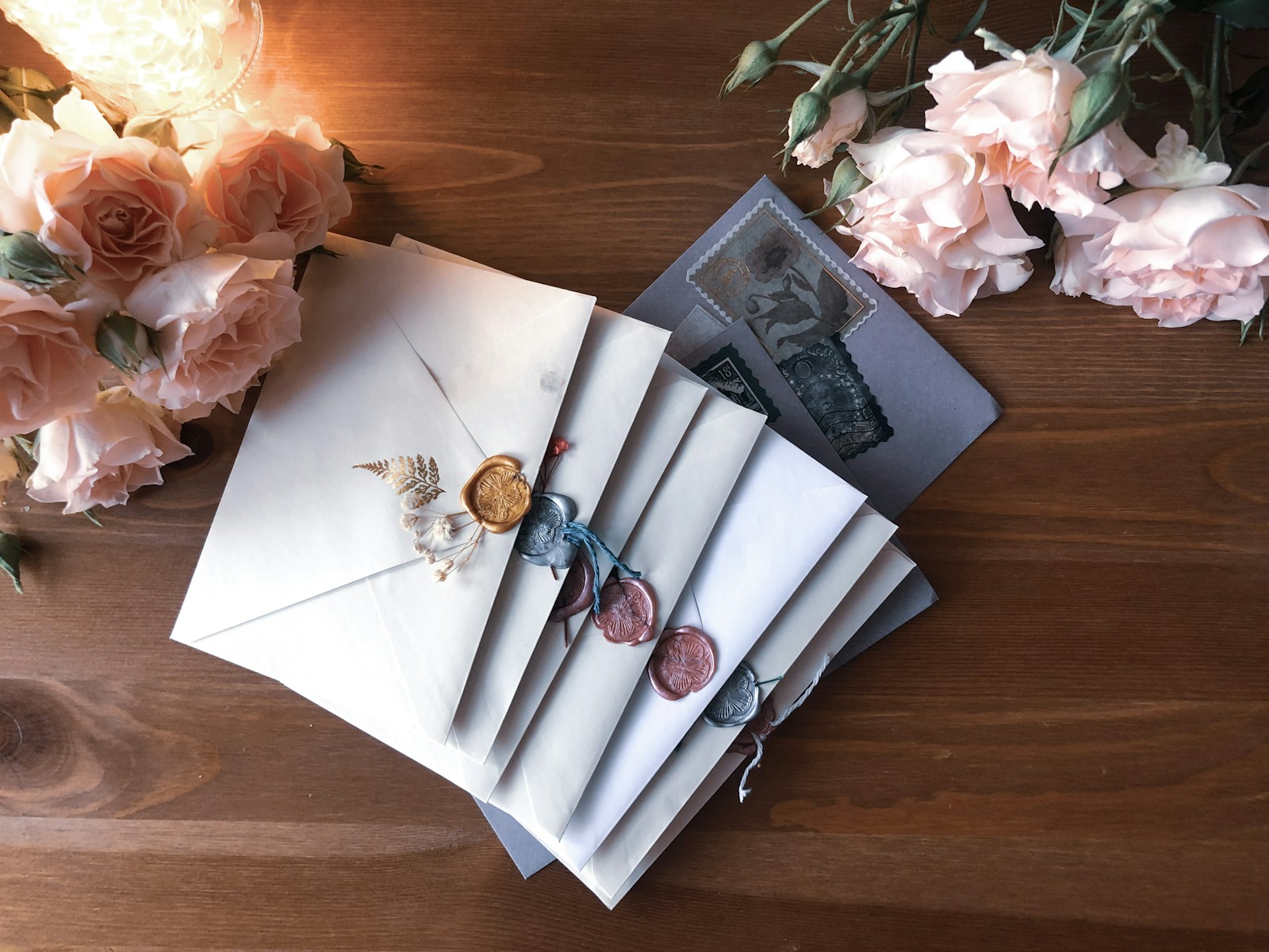 Envelopes sealed with coloured wax beside pale pink roses on a wooden table
